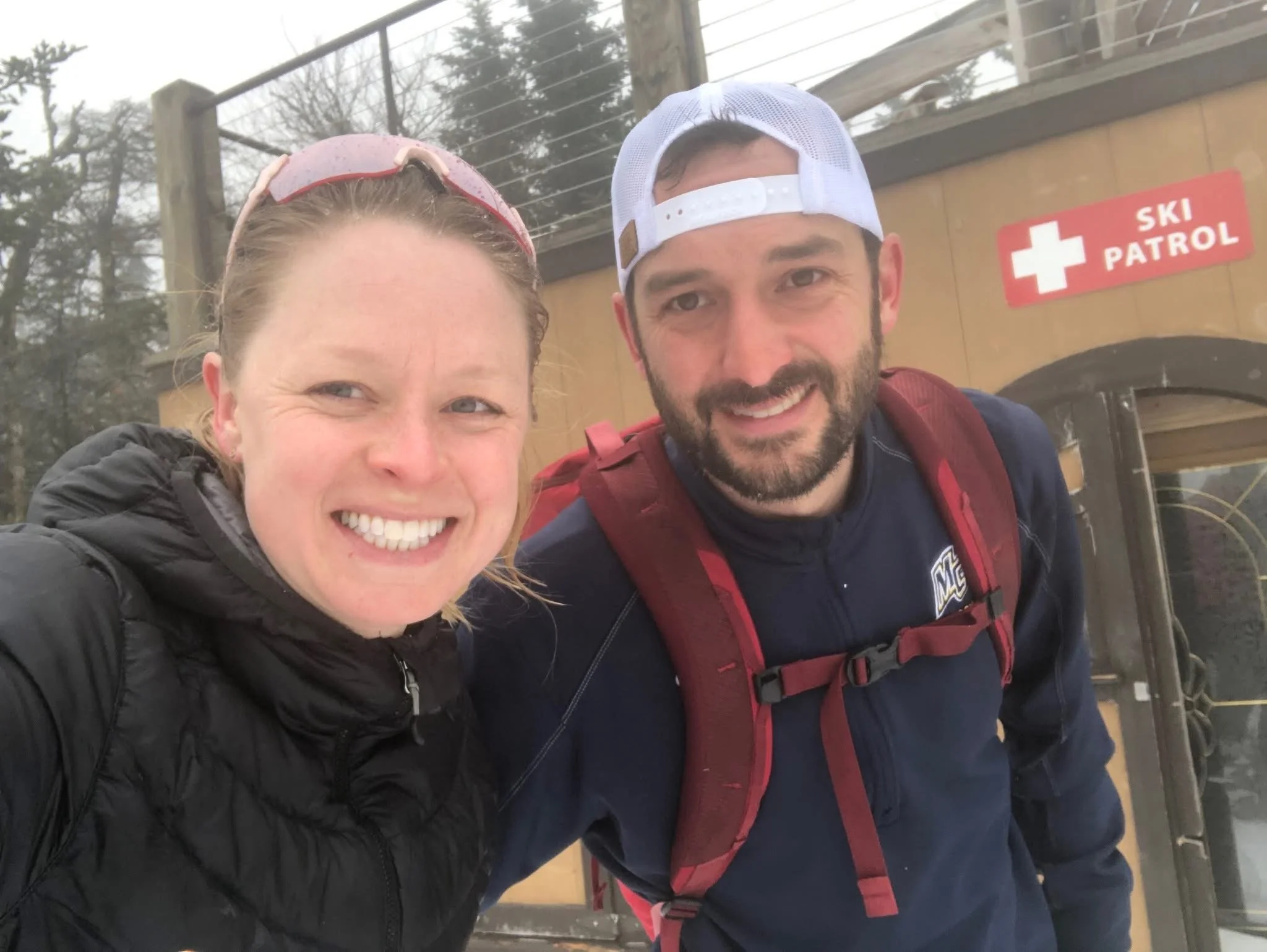 Matt Pimentel co-founder at the top of the mountain after uphill skiing with the ski patrol hut in the background.