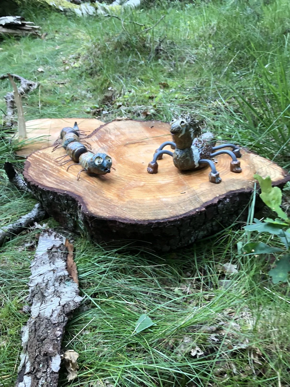 Kunstige insekter og dyr lavet af materialer på en træstamme i en grøn skov.