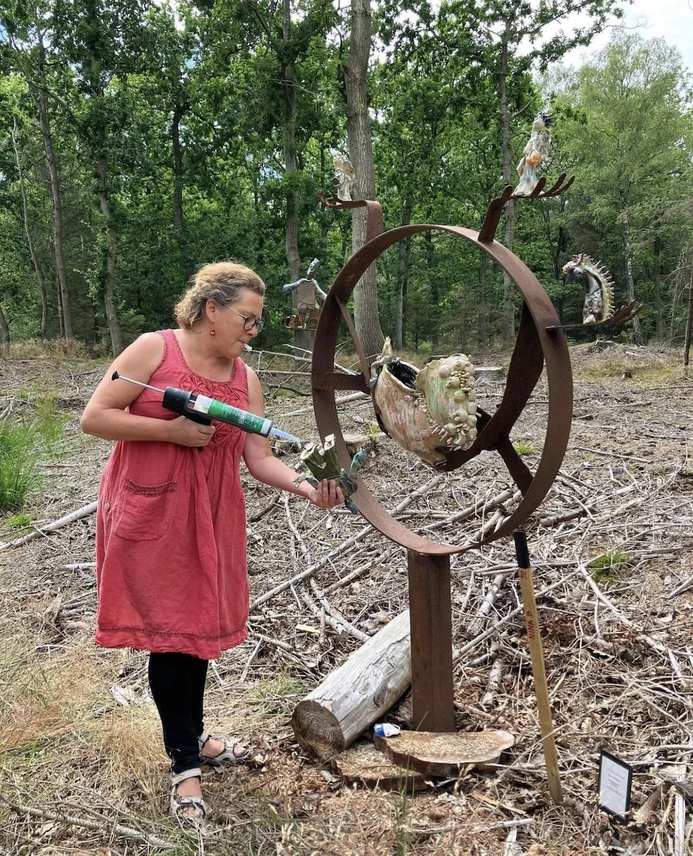 Kvinde med rød kjole, der arbejder på en skulptur i en skov.