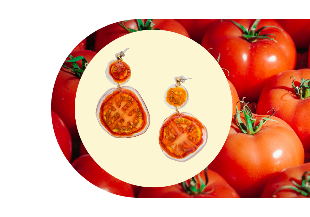 A pair of earrings made from tomatos, placed against a background of ripe red tomatoes.