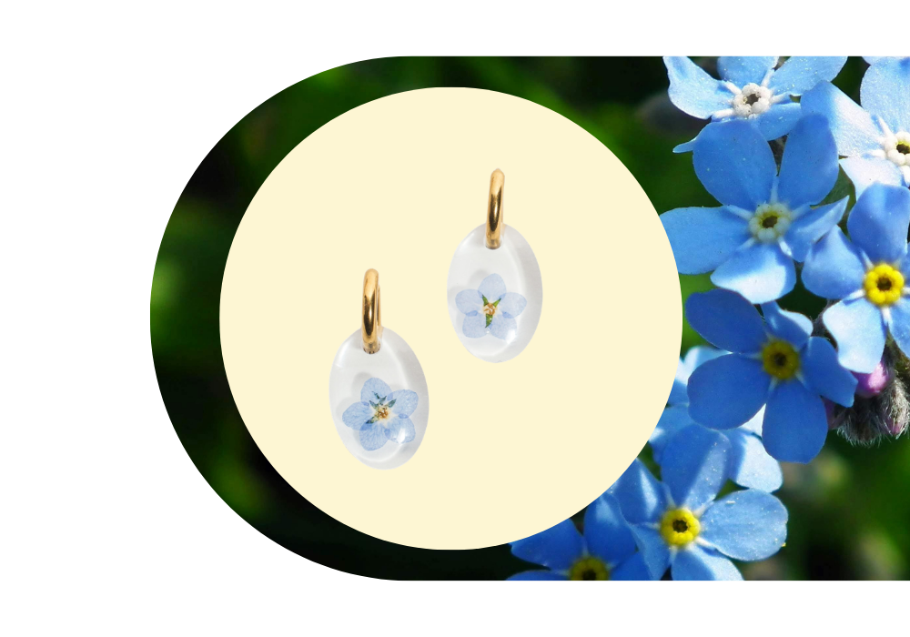 Gold hoop earrings with blue forget-me-not flower pendants on a pale yellow background, surrounded by a cluster of blue forget-me-not flowers.