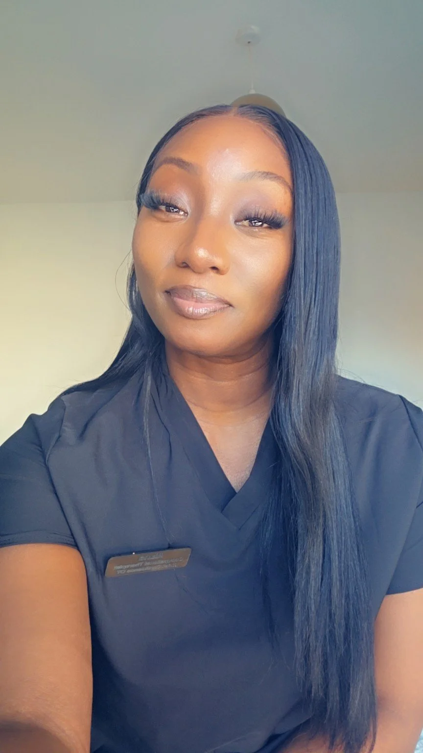 Close-up of a woman with long black hair and makeup, wearing a black top, in a well-lit room.