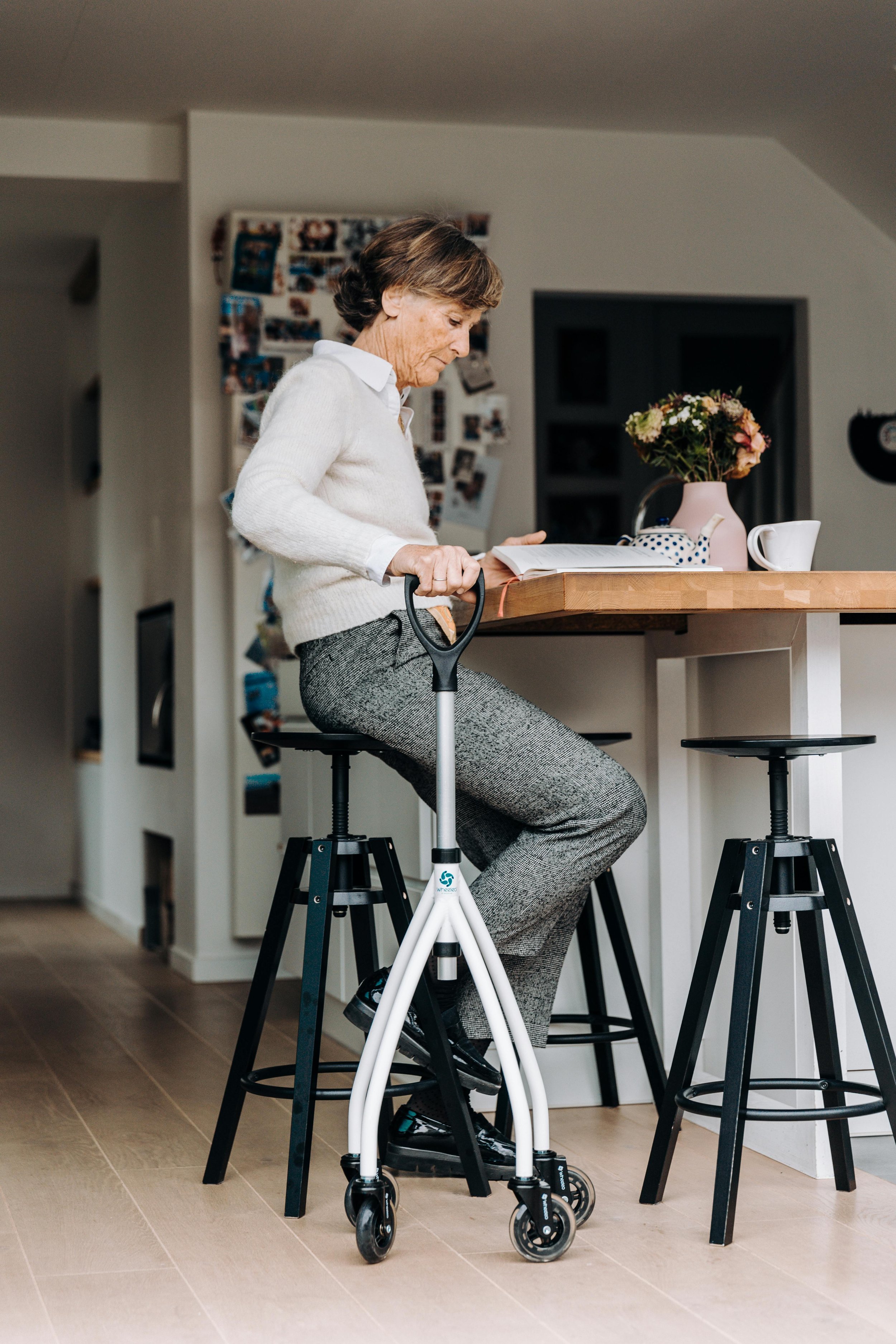 An elderly woman sitting on a high stool at a kitchen island, using a walker.