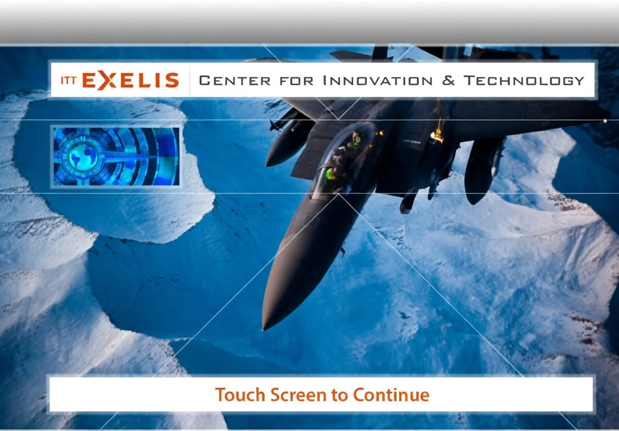Screenshot of the ITT EXELIS Center for Innovation & Technology with a fighter jet flying over icy mountains, and a digital interface display on the left, with the text 'Touch Screen to Continue' at the bottom.