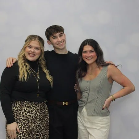 Three people smiling and posing together in front of a custom backdrop at a graduation party in norwalk ohio.