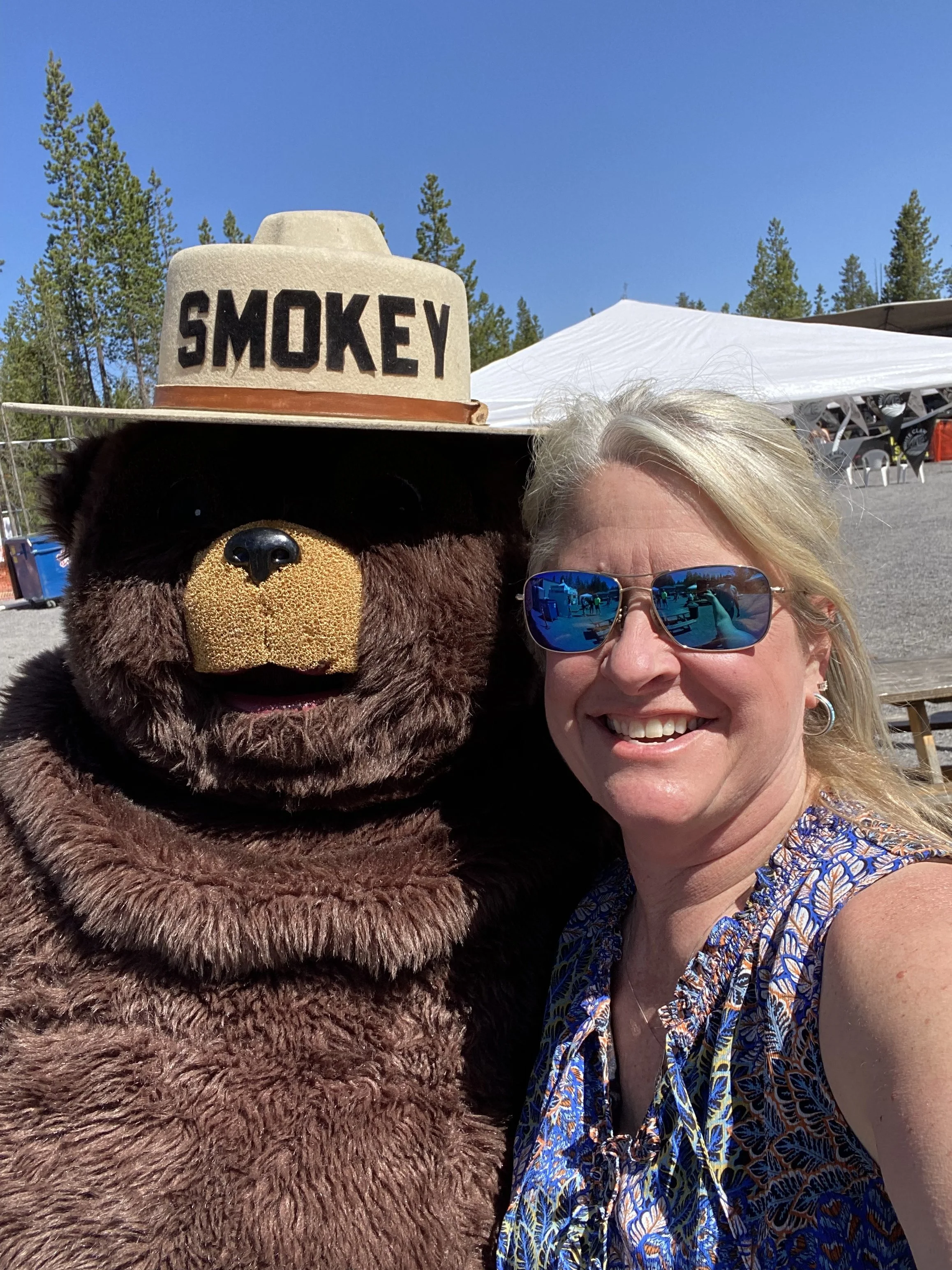 A woman taking a selfie with a Smokey the Bear outdoors.