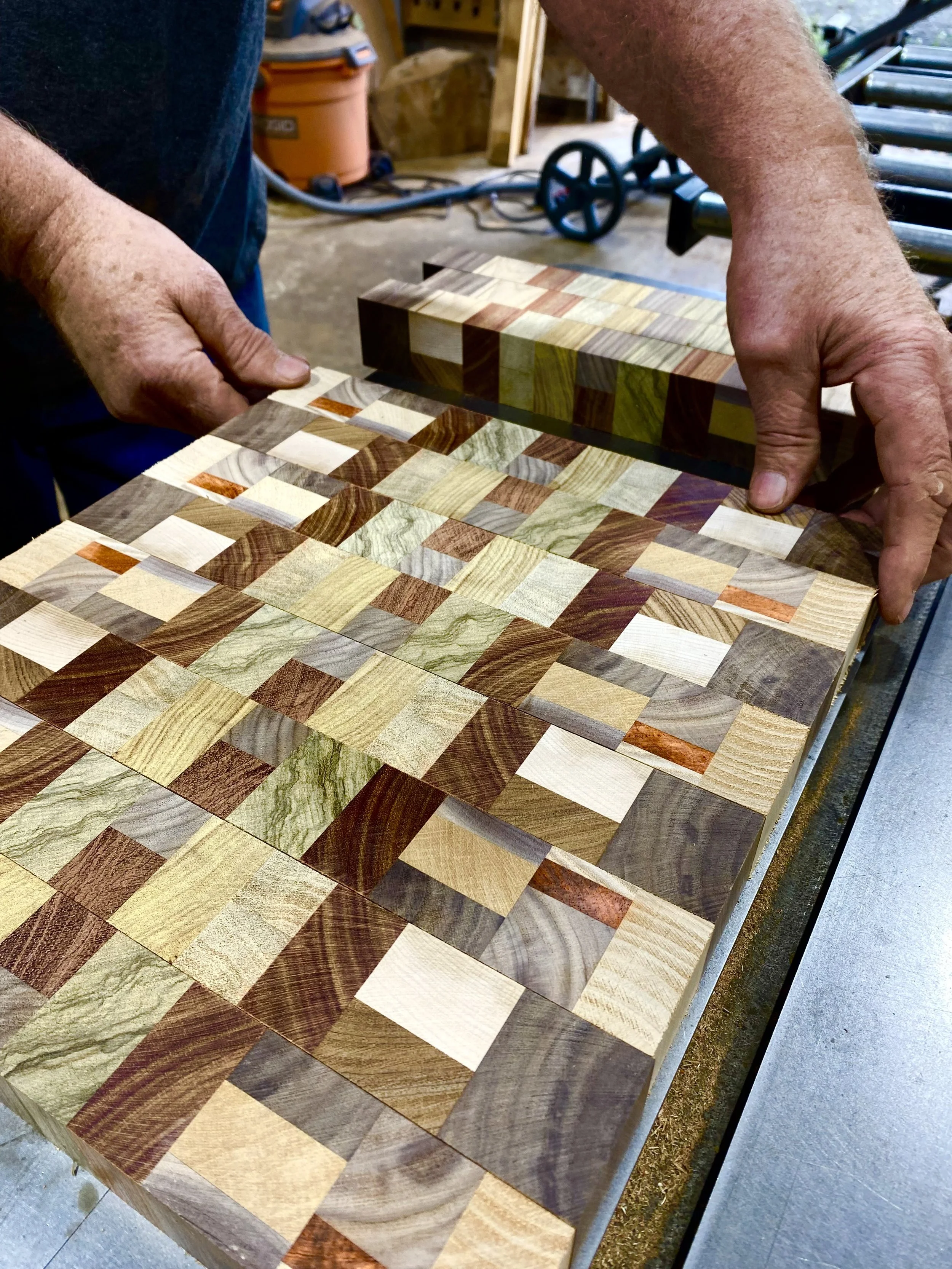 A person working on a multi-colored wooden checkerboard charcuterie in a workshop.