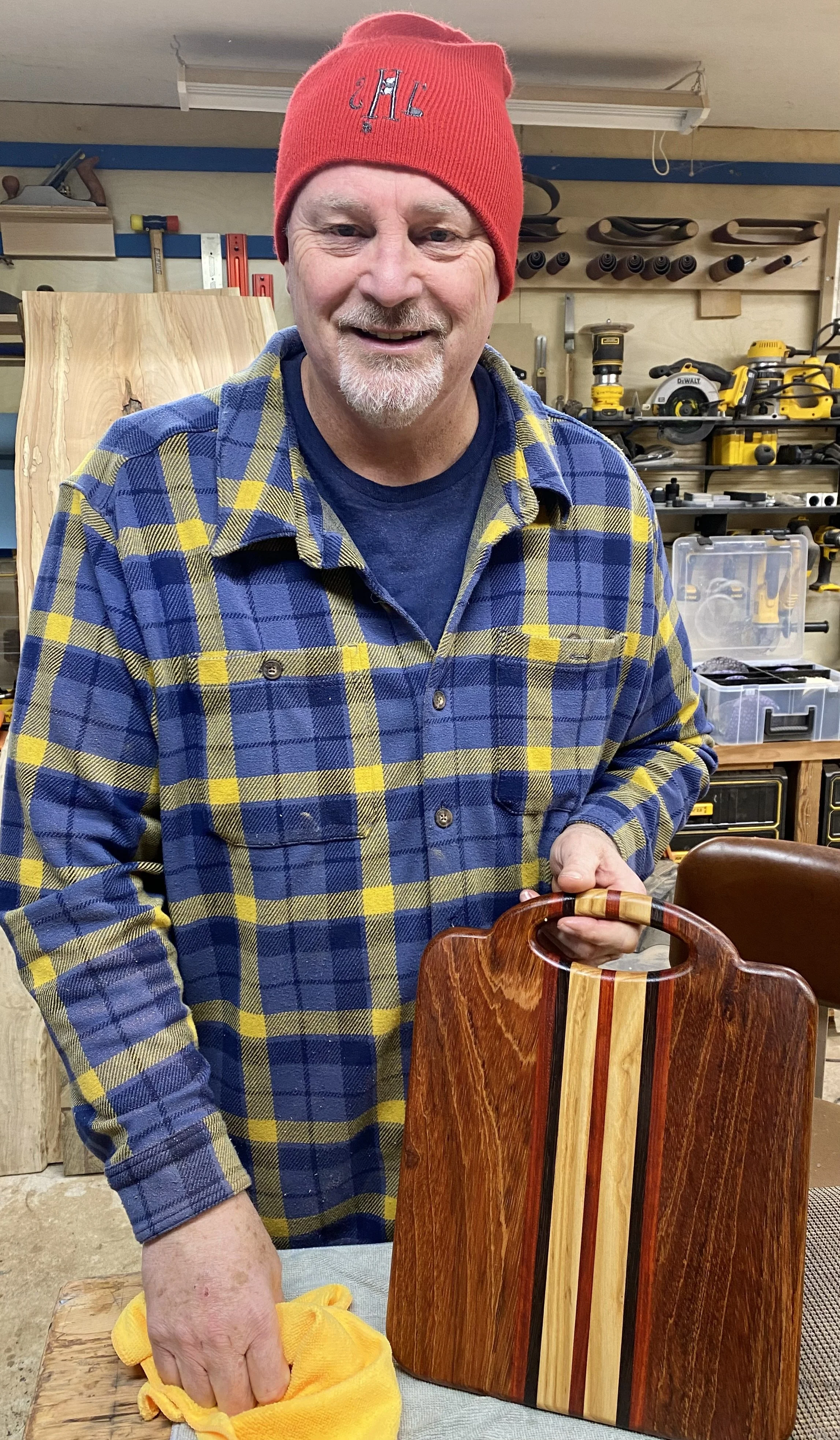 A man holds a polished handmade wooden cutting board with a decorative inlay.