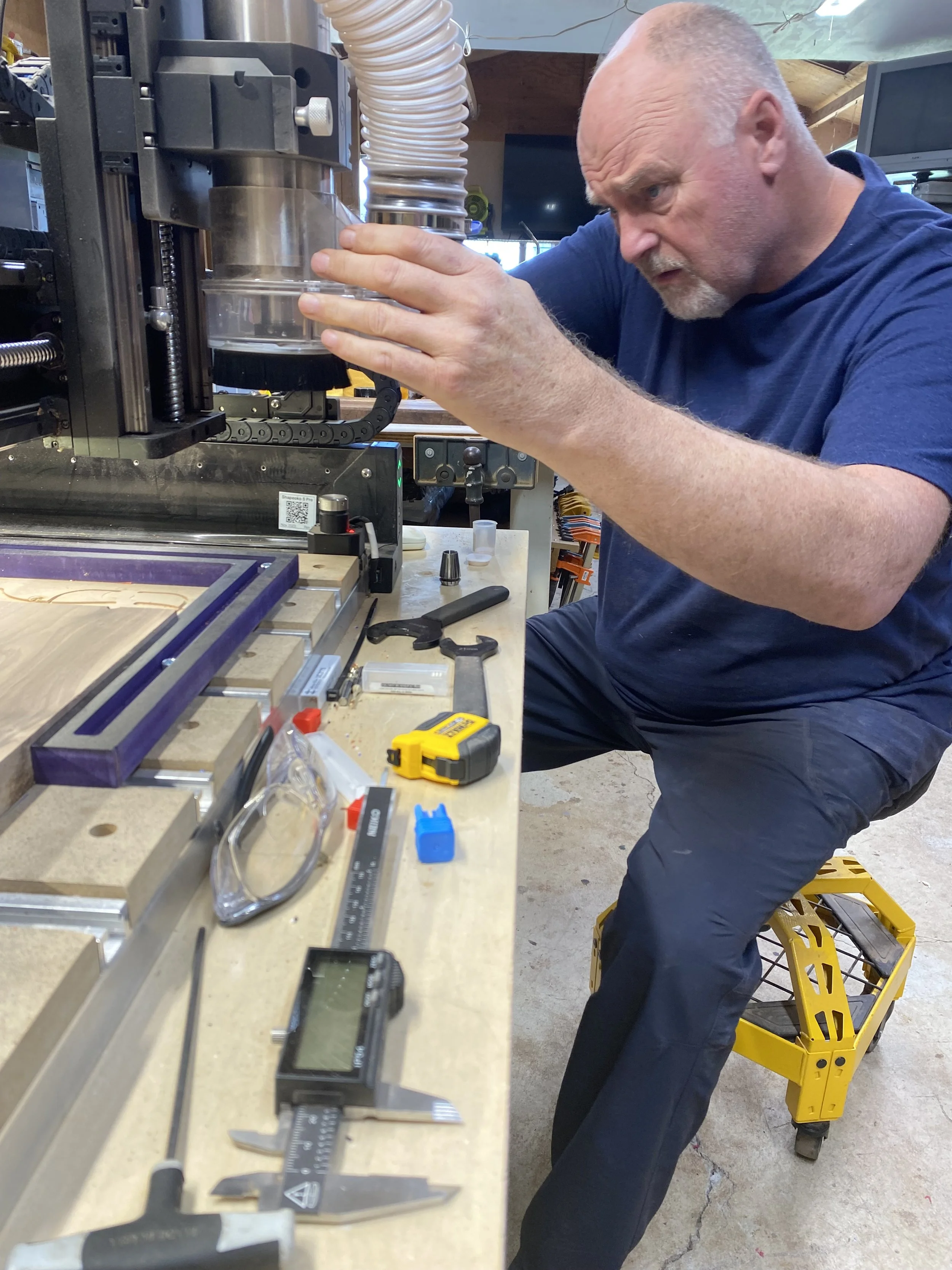 A man working on a precision machine in a workshop, focused on custom woodwork.