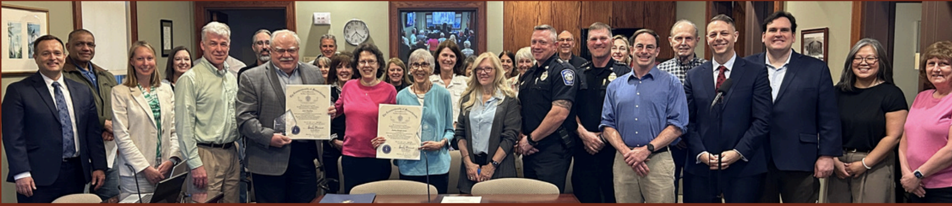 Group of people gathered in a room, some holding certificates, for a celebratory event. Four police officers are present, and everyone is smiling.