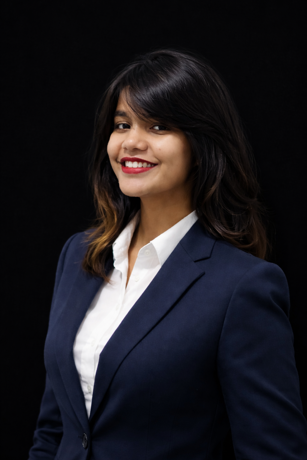 Portrait of a young woman with shoulder-length dark hair, wearing a navy blue blazer and white shirt, smiling against a black background.