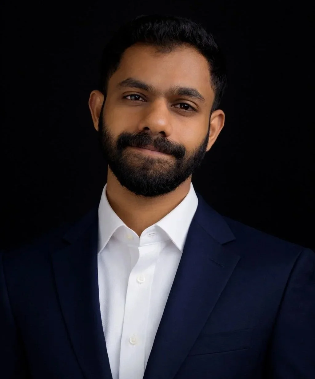 A man with a beard and mustache in a suit and white dress shirt, against a black background.