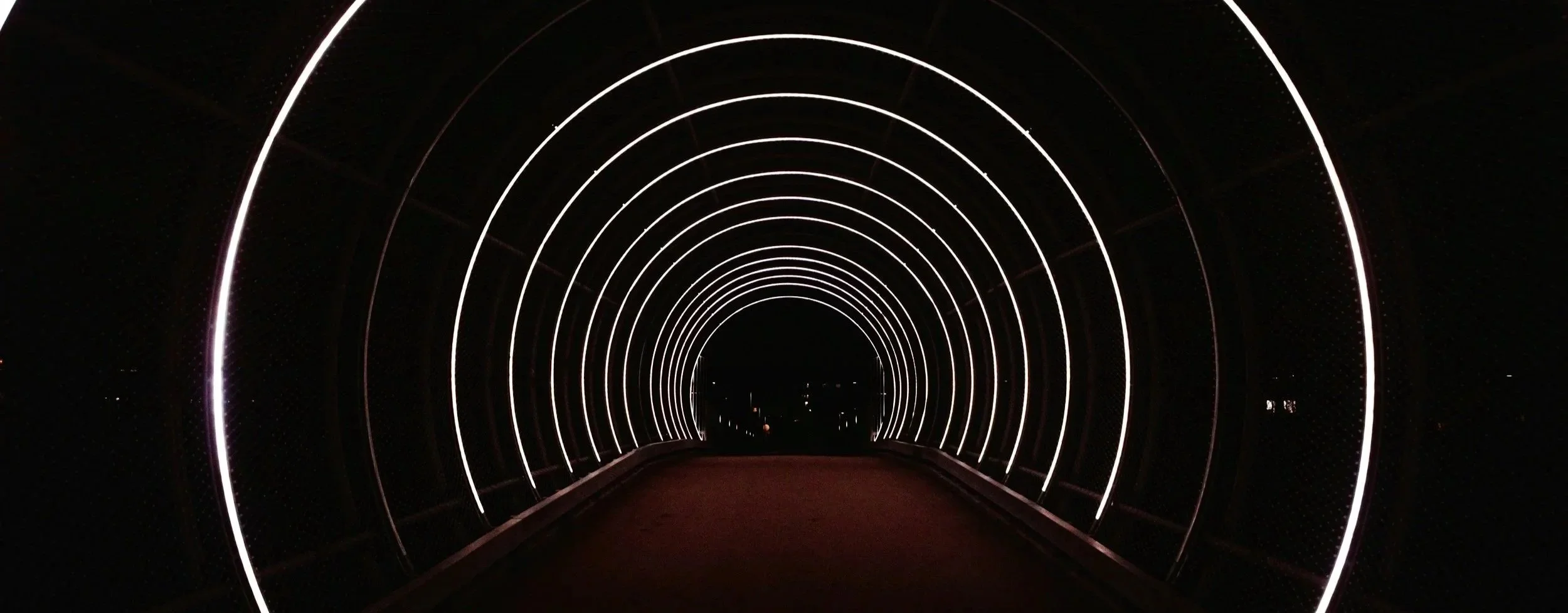 Nighttime view through an illuminated tunnel with concentric circles of white lights.