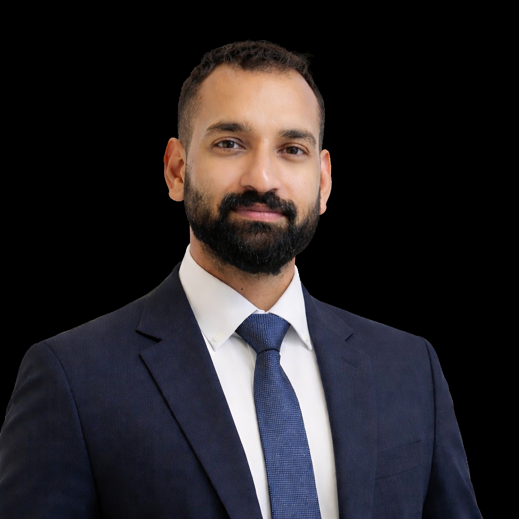 A man in a dark suit, white shirt, and blue tie against a black background.