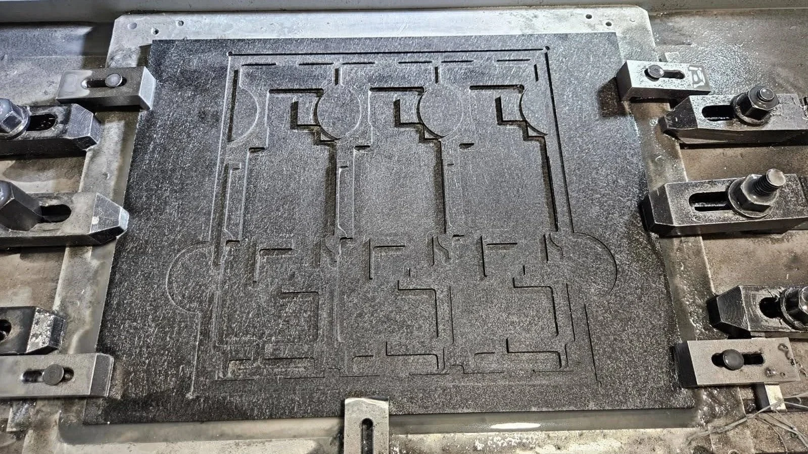 Metalworking mold with engraved patterns, surrounded by metal clamps.