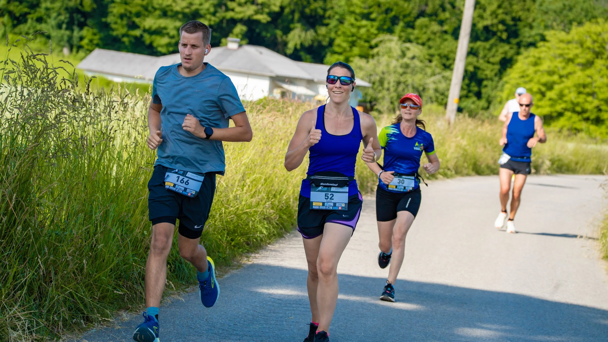 Mehrere Läufer beim Marathon auf einer ländlichen Straße mit grüner Landschaft und bunten Turnschuhen, männlich und weiblich, im Training oder Wettkampf