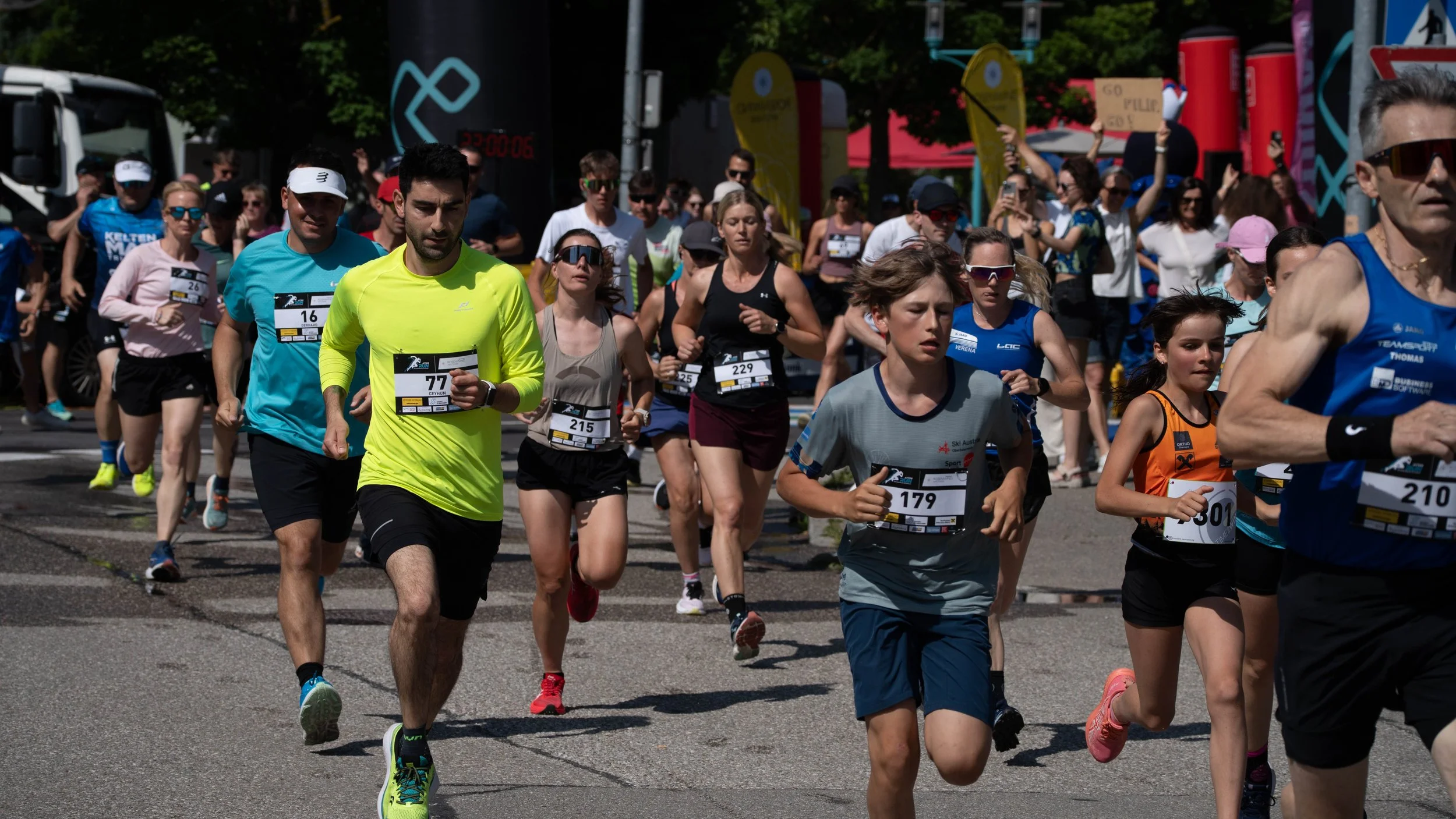 Menschen laufen bei einem Stadtmarathon auf der Straße, viele tragen Laufkleidung und Nummern, im Hintergrund befinden sich Zuschauer und Banner.