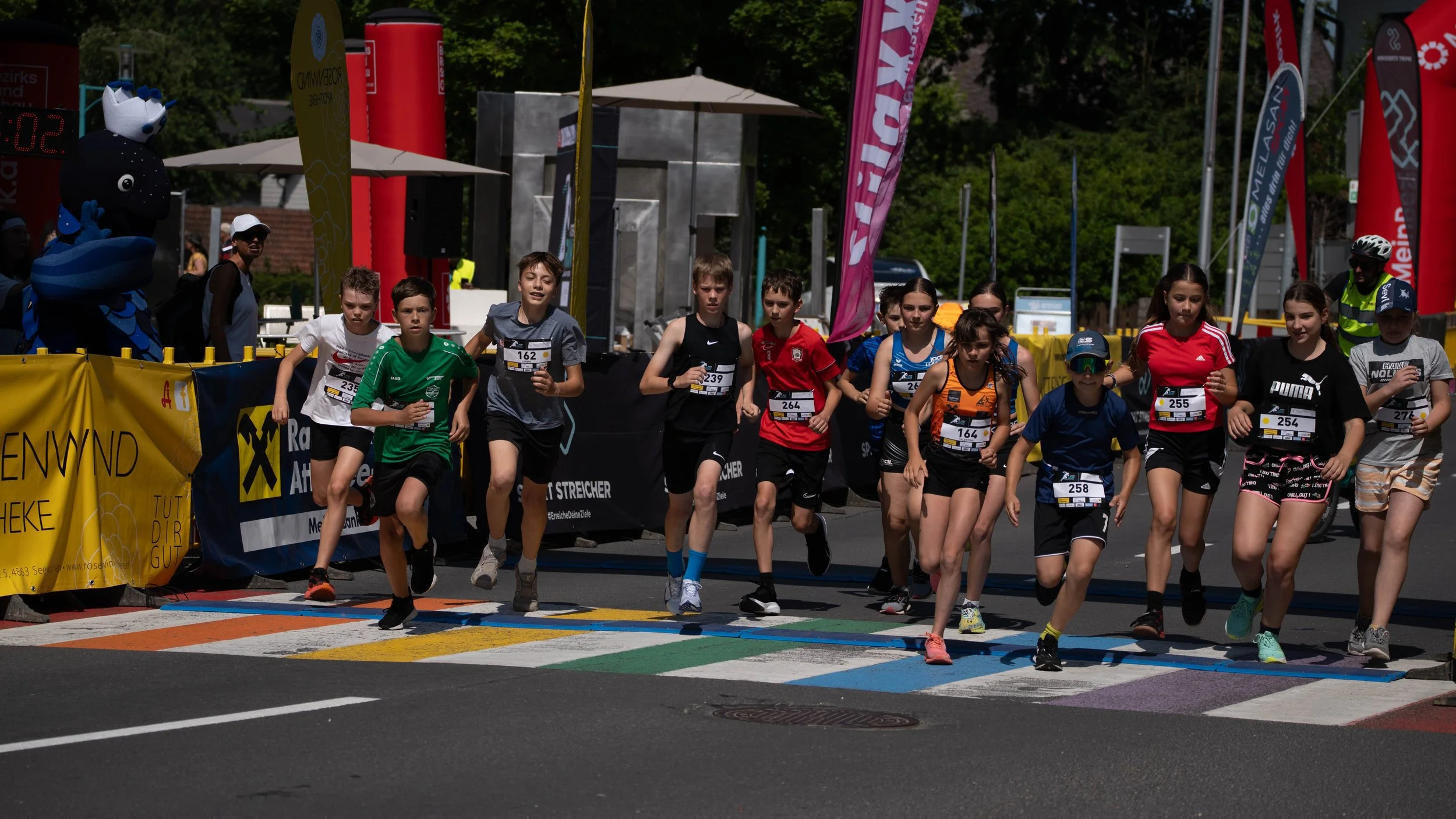 Jugendliche beim Start eines Crosslauf-Wettbewerbs, die eine bunte Startlinie überqueren.