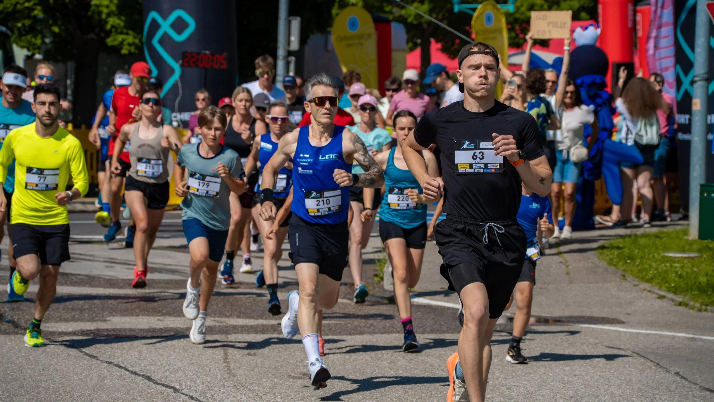 Läufer beim Marathonlauf auf der Straße, Zuschauer im Hintergrund, sonniger Tag.