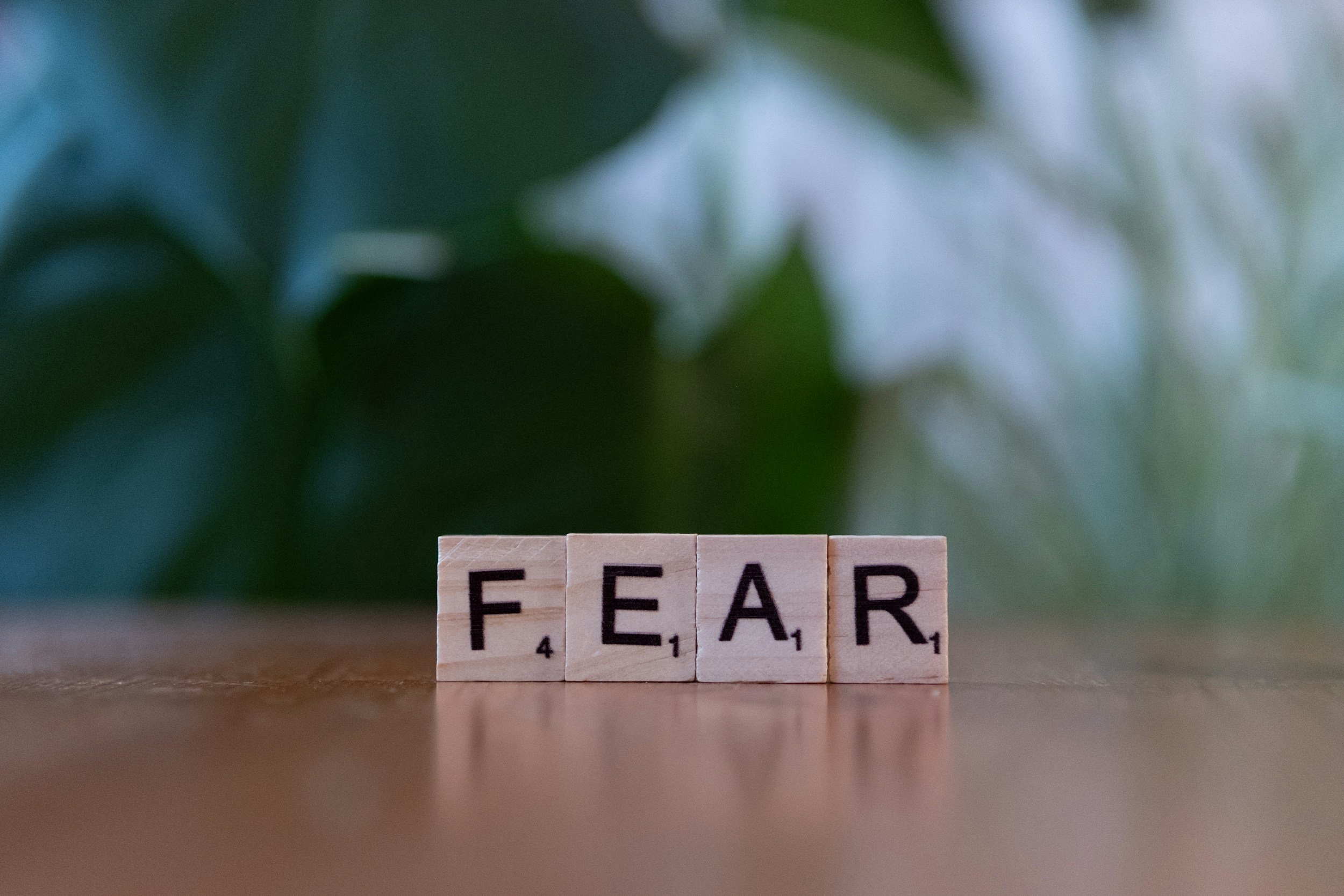 Scrabble tiles spelling out 'FEAR' on a wooden surface with green leaves blurred in the background.