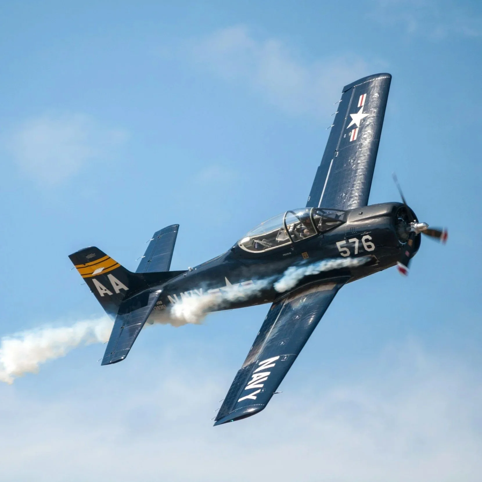 A black fighter jet with NASA and military markings flying through the sky, leaving smoke behind.