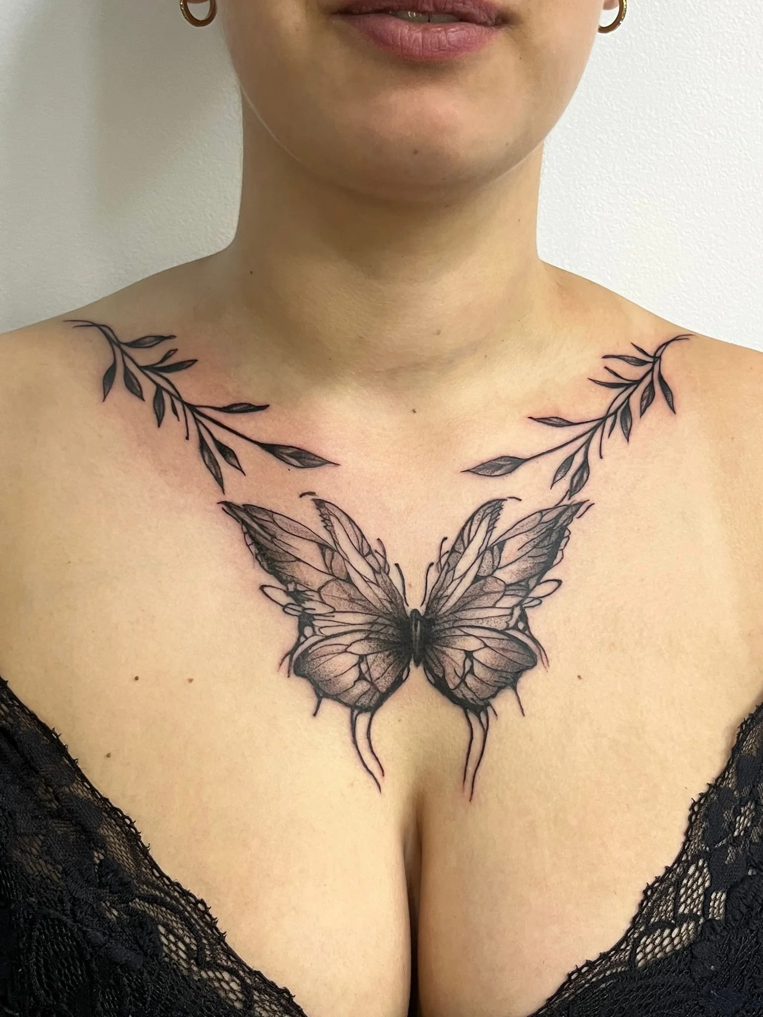 Tatuagem de uma borboleta e ramos de folhas no colo de uma mulher