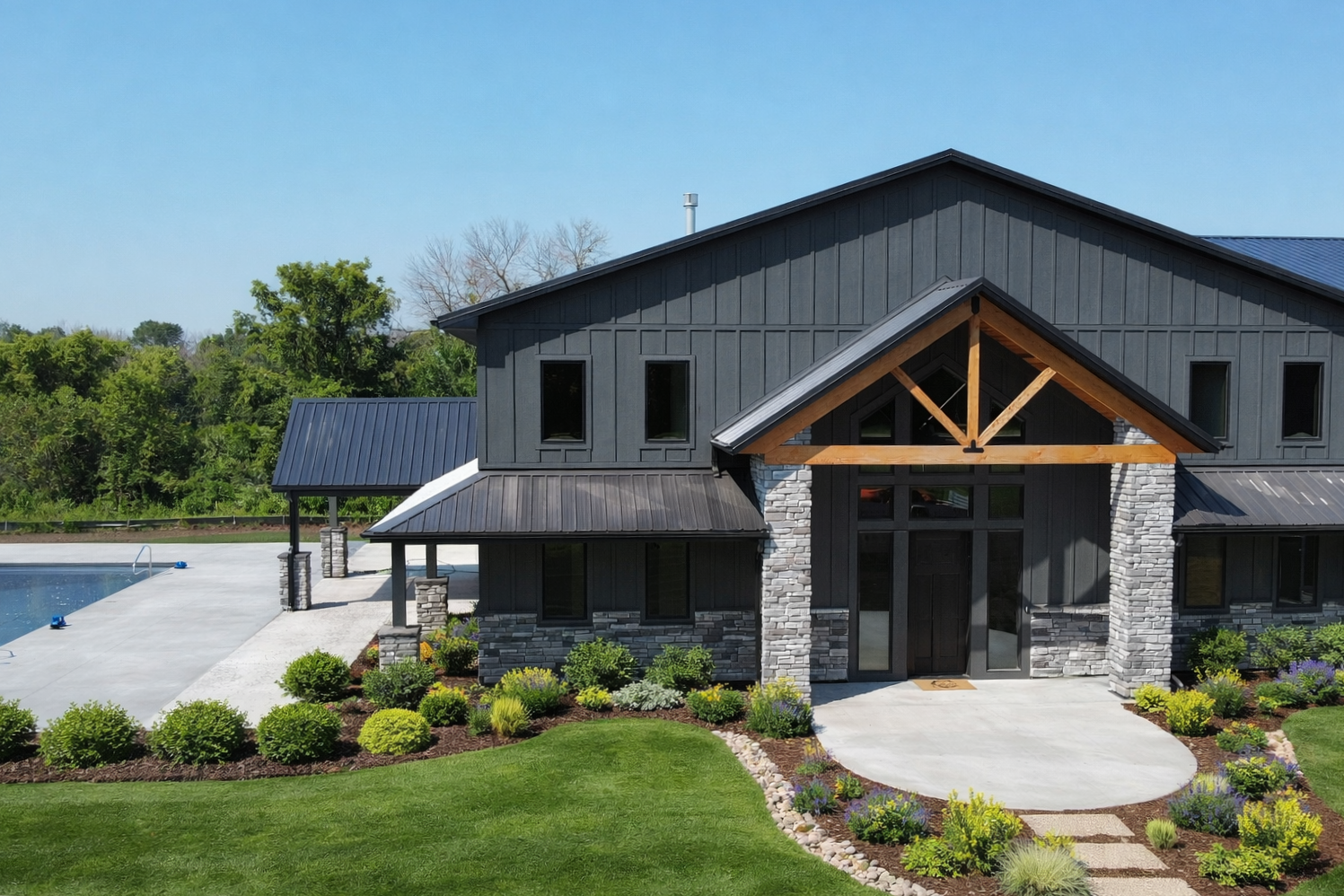 Landscaped custom barndominium by Sprengeler Construction featuring modern rustic design, stone accents, manicured lawn, and curated front entry plantings