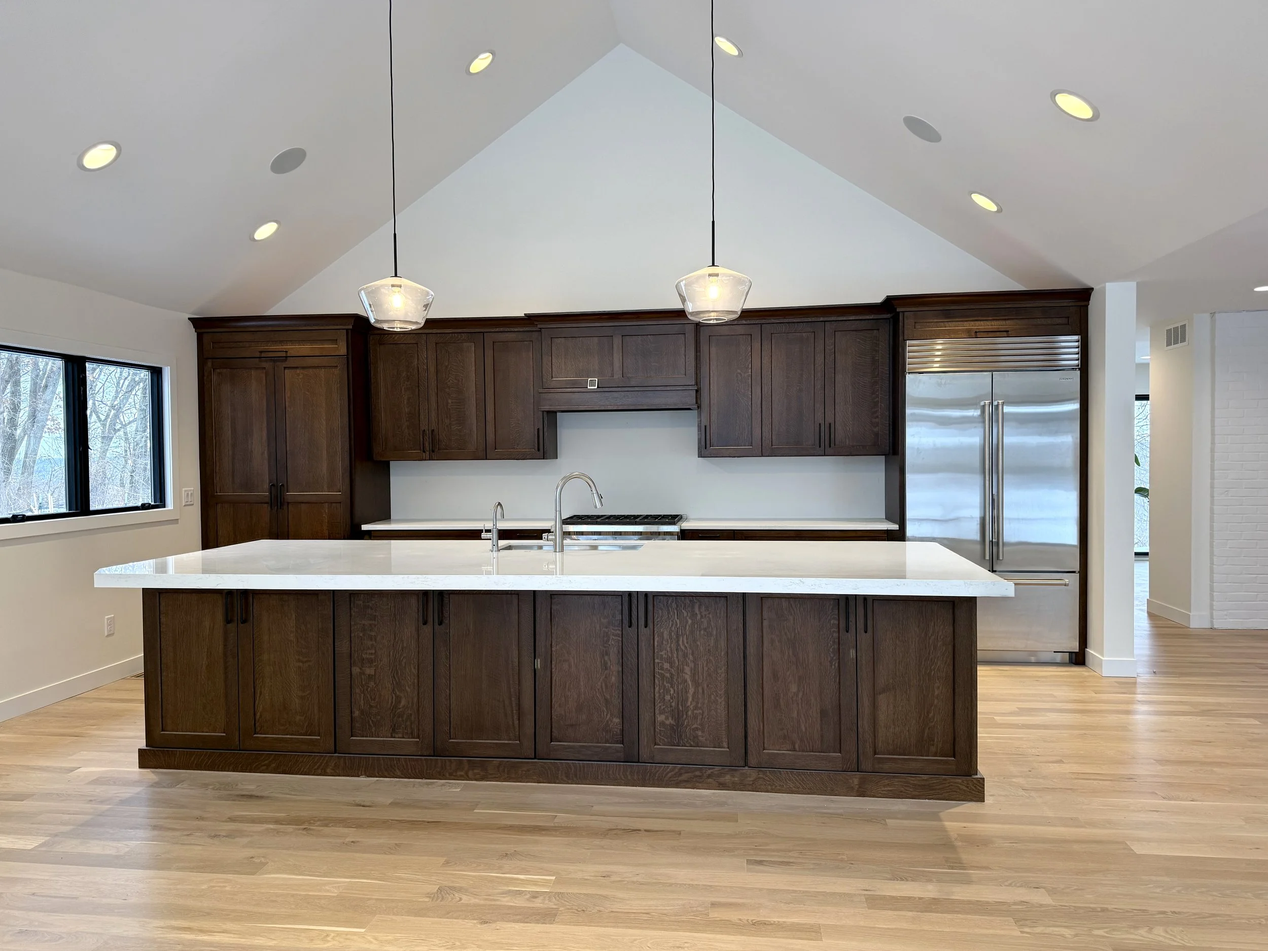 Custom kitchen by Sprengeler Construction featuring dark wood cabinetry, large island, quartz countertops, vaulted ceiling, and modern pendant lighting