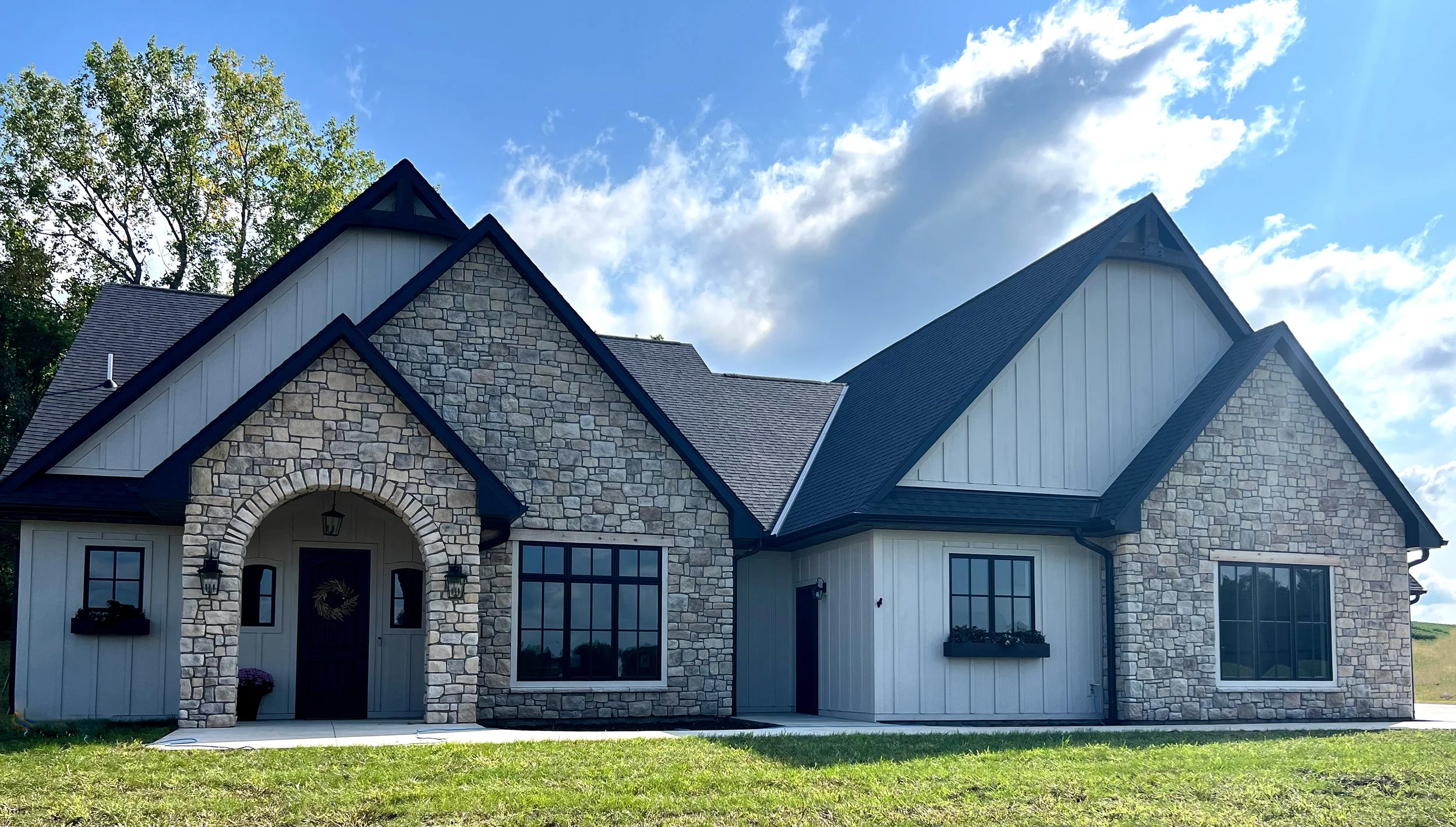 Custom modern farmhouse by Sprengeler Construction featuring stone exterior, gabled rooflines, arched entry, and large windows with natural light