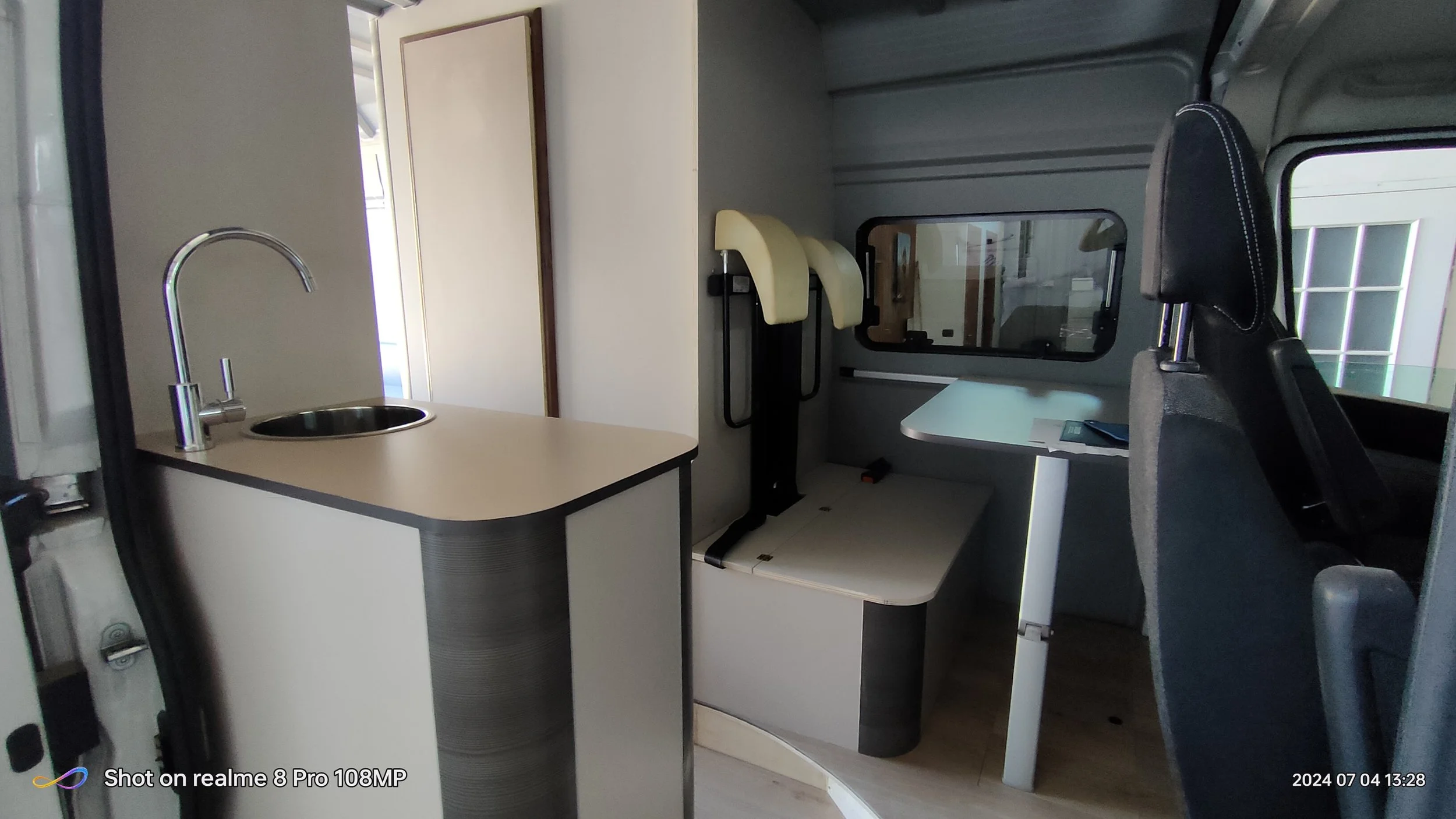 Interno di un camper con cucina, sedile e finestra.