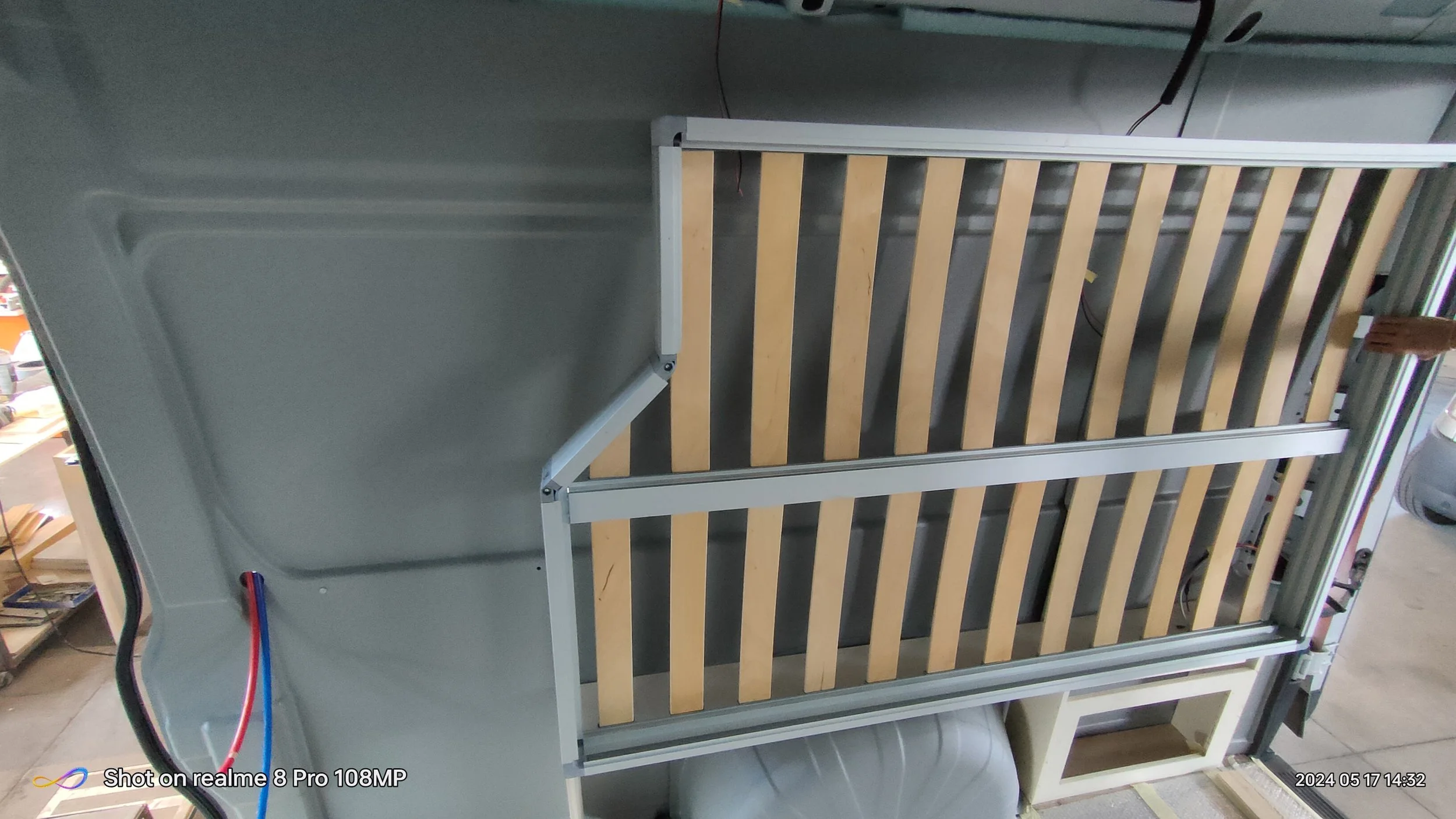 Immagine di una struttura metallica e in legno, probabilmente un letto con una testiera e una pediera in legno, con alcune parti elettriche visibili.