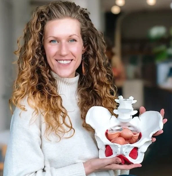 Woman smiling and holding a plastic model of a pelvis with uterus inside it.