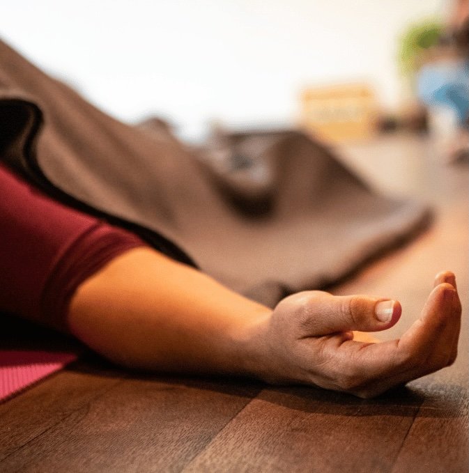 Close-up of a person lying on a yoga mat with their arm extended and hand relaxed in a meditation pose.