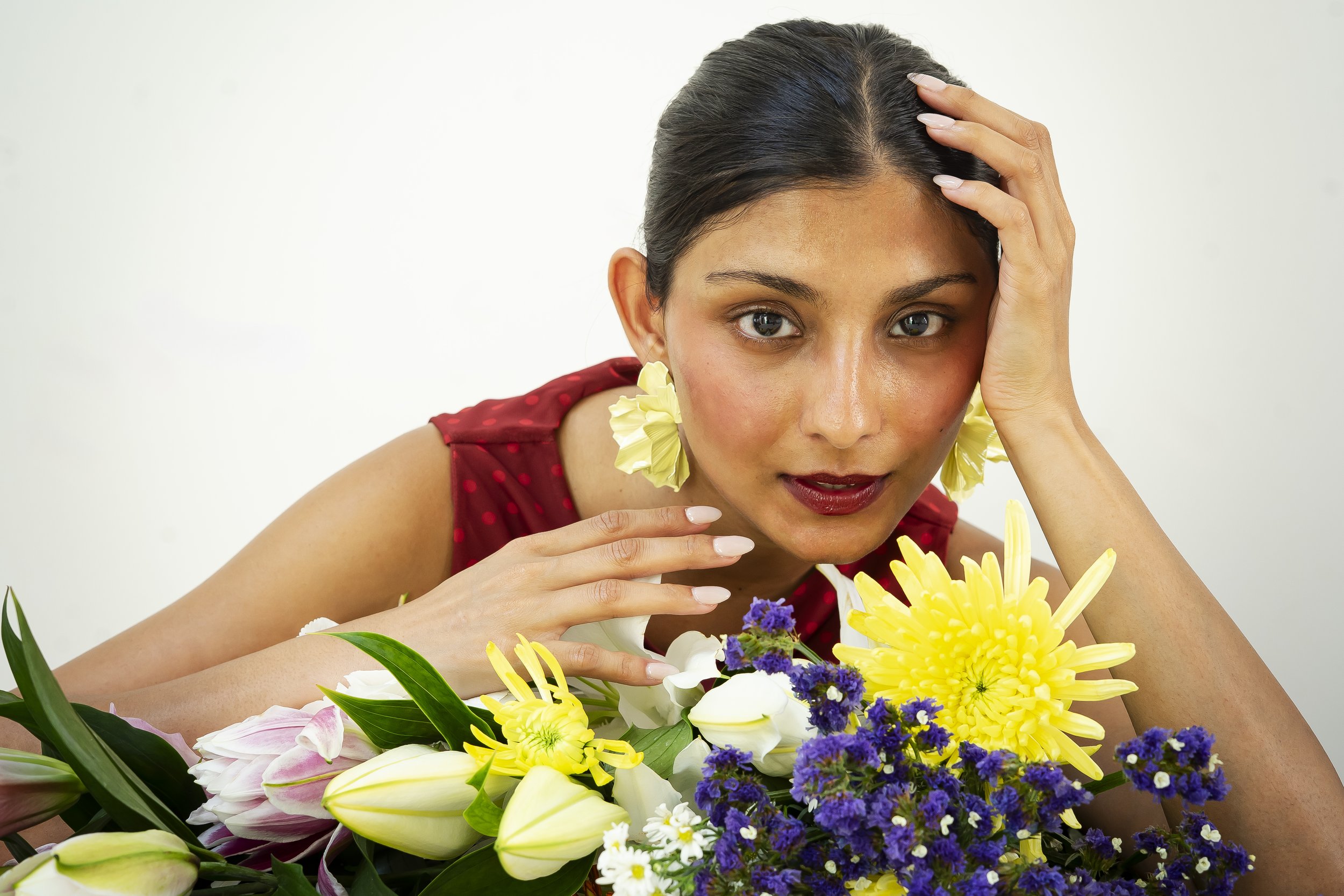 A woman with dark hair and light skin resting her head on her hand, surrounded by colorful flowers.