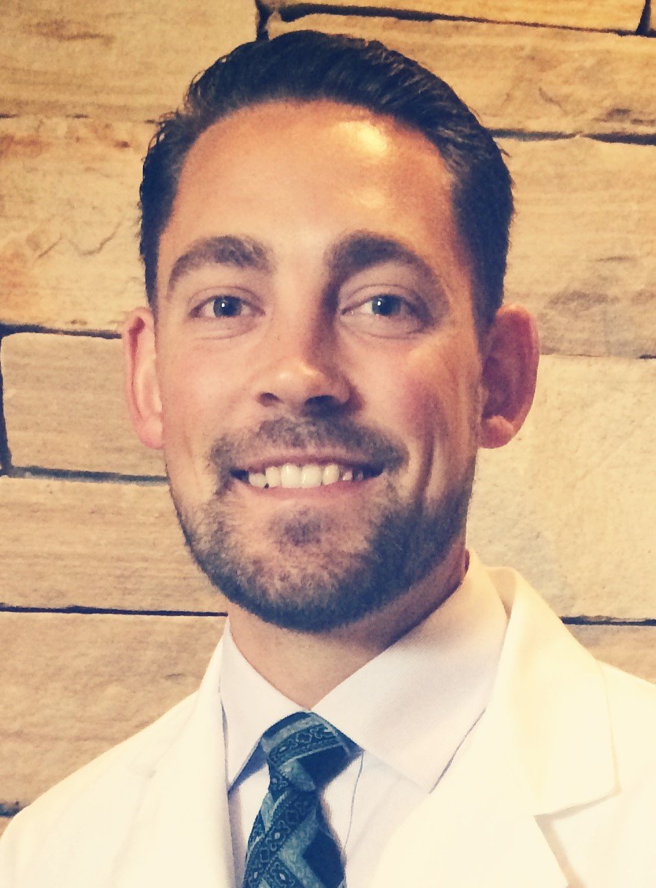 Dr. Jackson Bell in a white suit and patterned tie, with a wooden wall background.