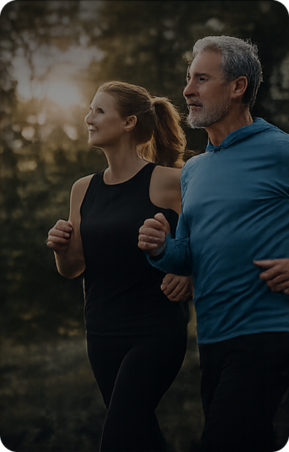 A man and a woman jogging outdoors during sunset in a forested area.