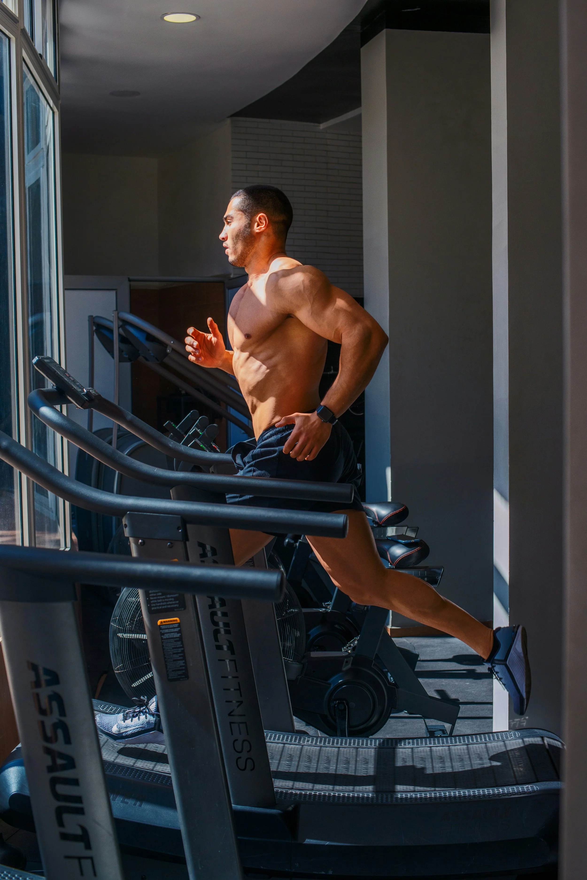 A shirtless man running on a treadmill inside a gym.