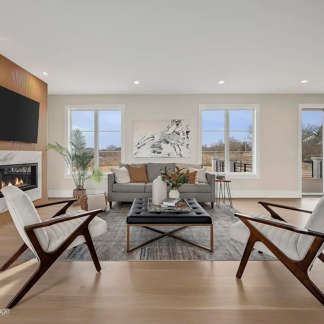 Modern living room with gray sofas, white armchairs, wooden flooring, fireplace, large windows, and contemporary artwork.
