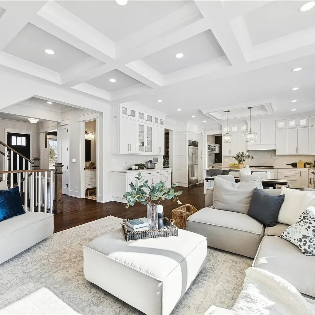 Open-concept living room and kitchen with white cabinetry, dark hardwood floors, and modern furniture, featuring a ceiling with tray details and recessed lighting.