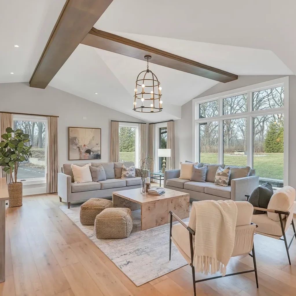 Living room with large windows, modern sofas, a rectangular coffee table, armchairs, a floor lamp, and houseplants in a bright, spacious interior.