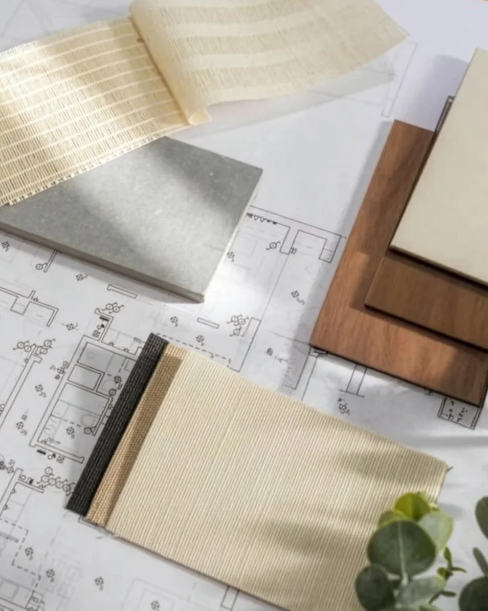 Sample interior design materials including fabric swatches, wallpaper samples, and a wooden flooring sample laid out on architectural blueprints.