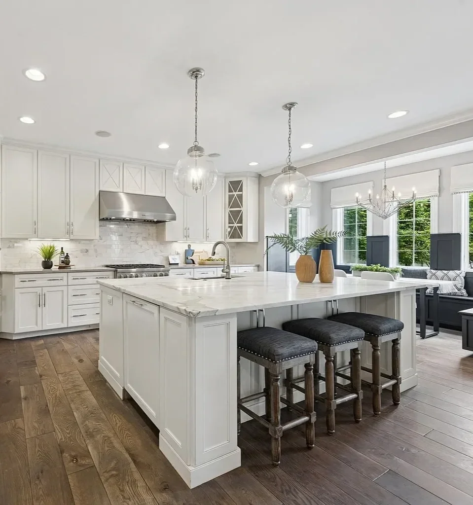 Bright, modern kitchen with white cabinets, a large central island, wooden stools, hardwood floors, and large windows.