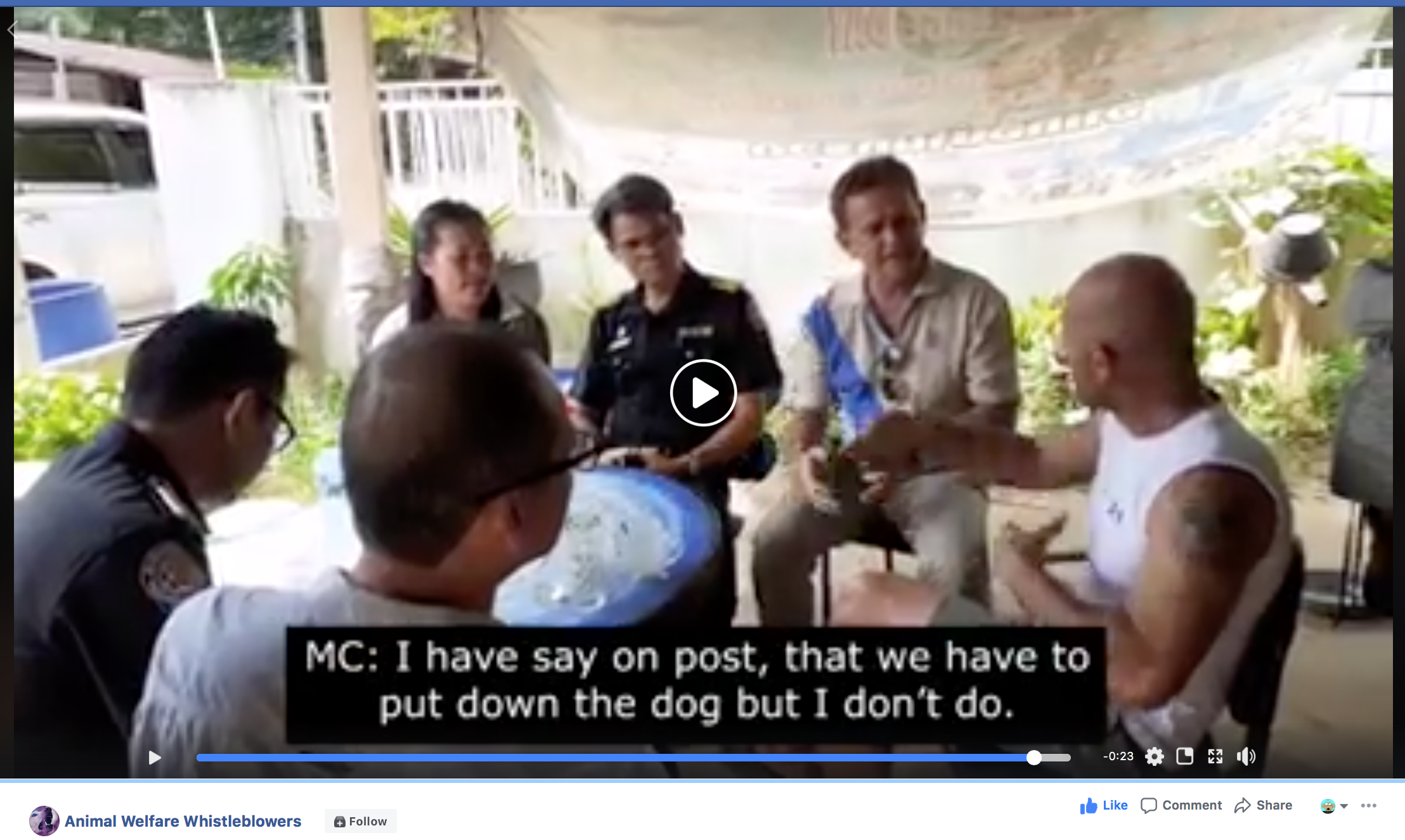 A group of people sitting outdoors, including a man with a tattooed arm in a white sleeveless shirt, discussion is taking place. Subtitles show one person says, 'I have say on post, that we have to put down the dog but I don't do.'