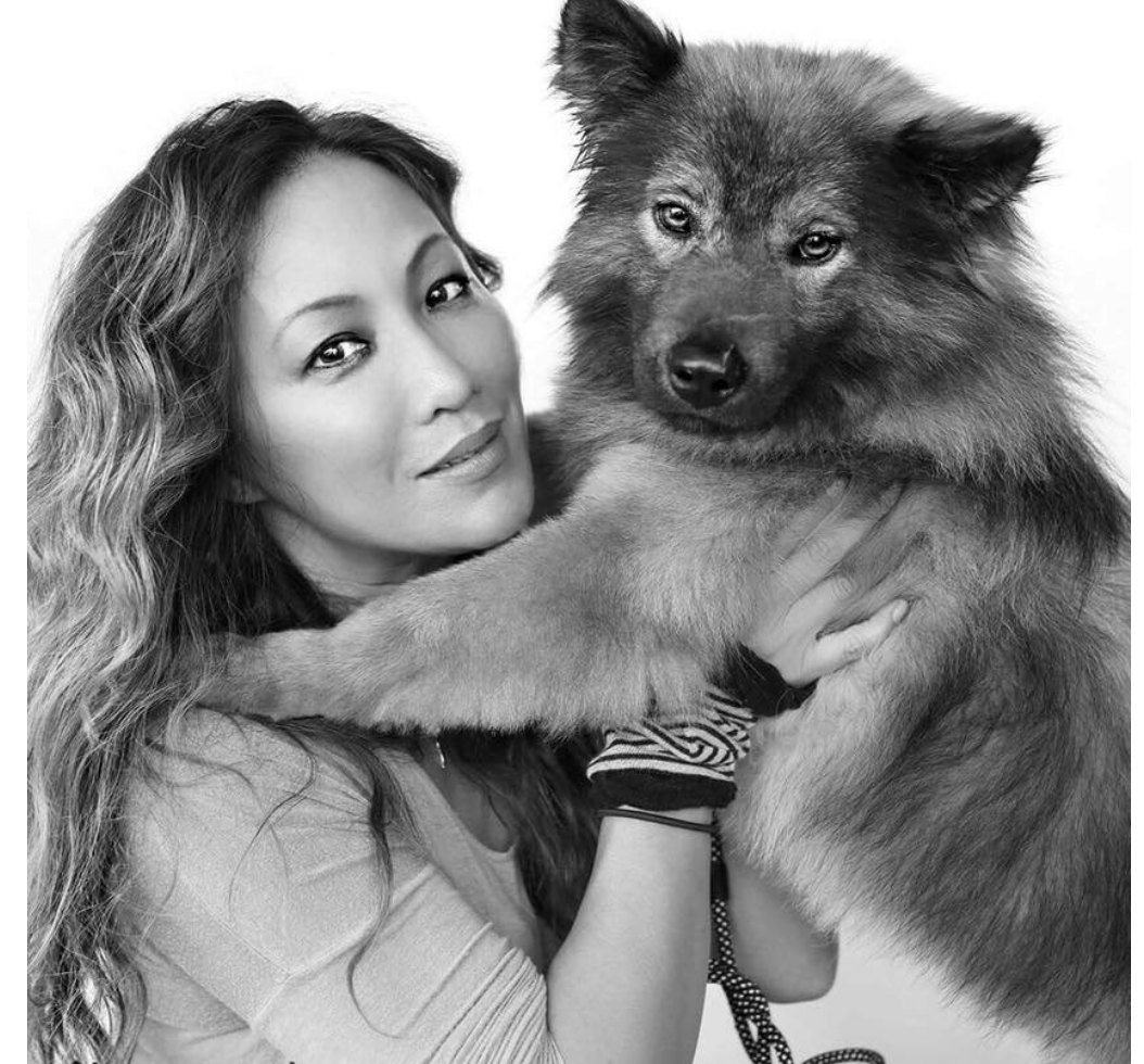 A woman with wavy hair holding a large fluffy dog with a thick coat, both looking towards the camera.