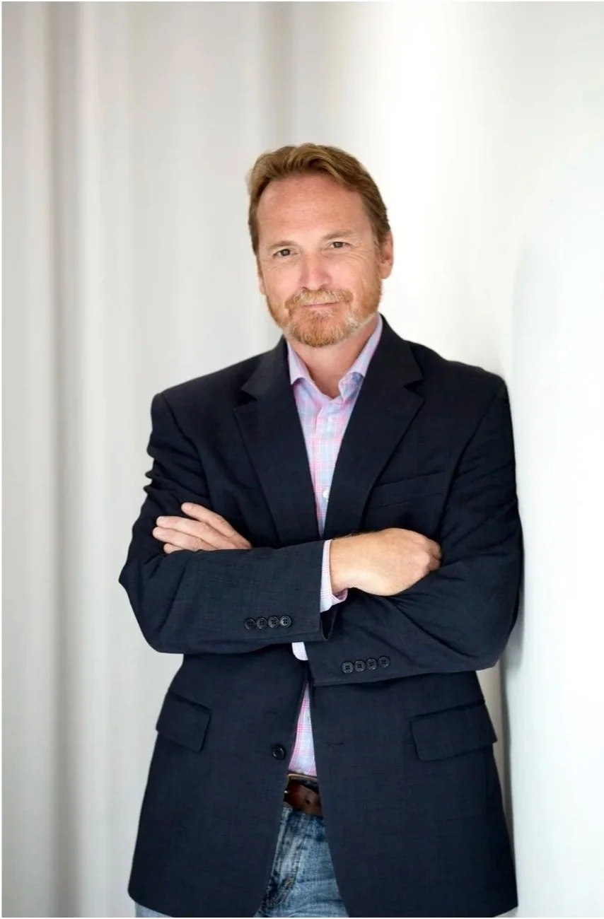 Gary Murrell, arms crossed, smiling, wearing a blazer and jeans against a light background.