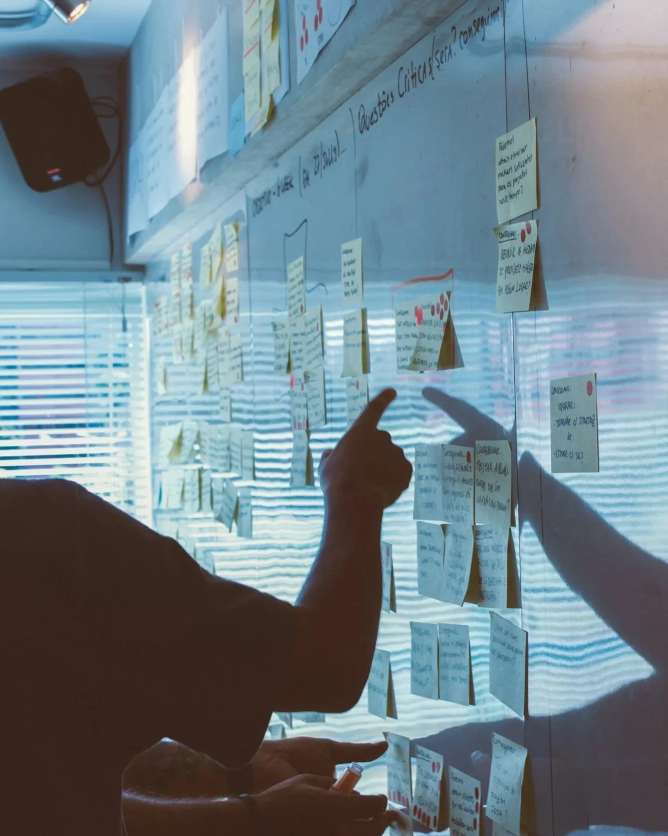 Pessoas discutindo e apontando para um quadro branco coberto de post-its com textos escritos.