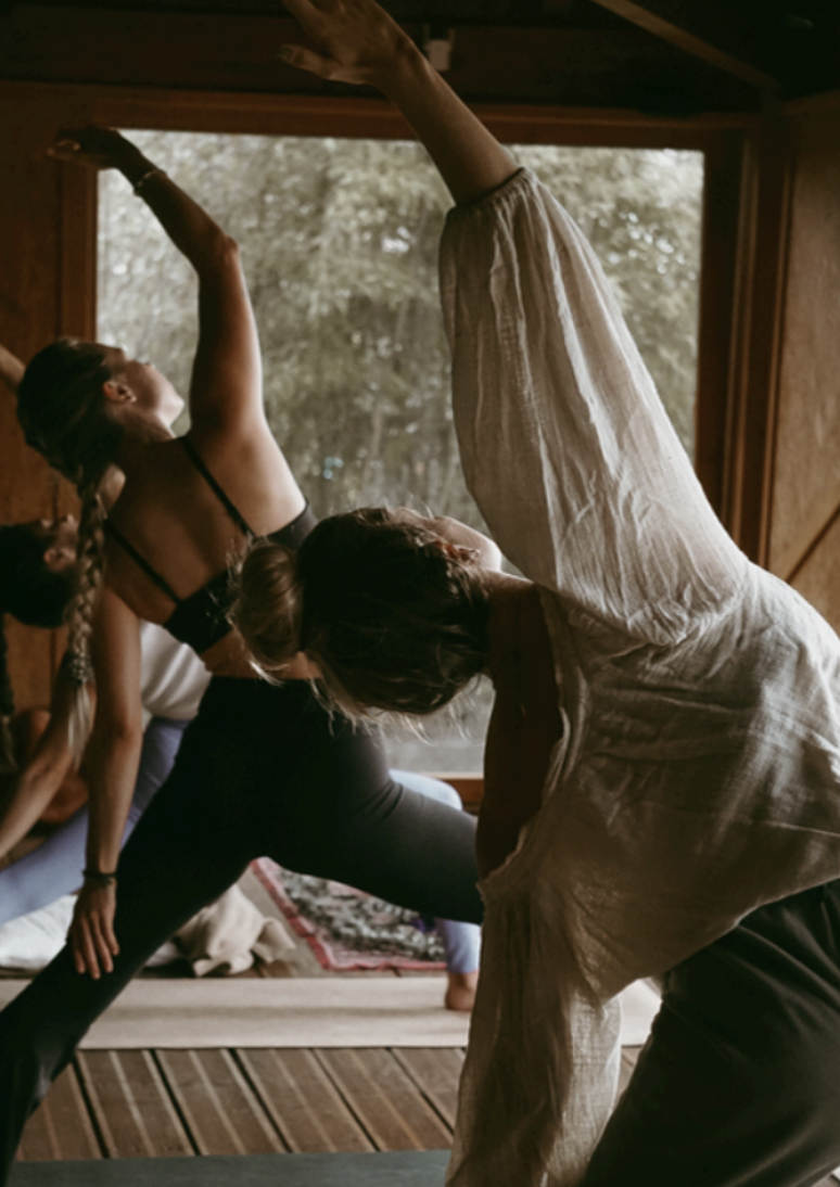 Grupo de pessoas fazendo yoga em um ambiente indoor, com janelas de vidro, durante o dia.