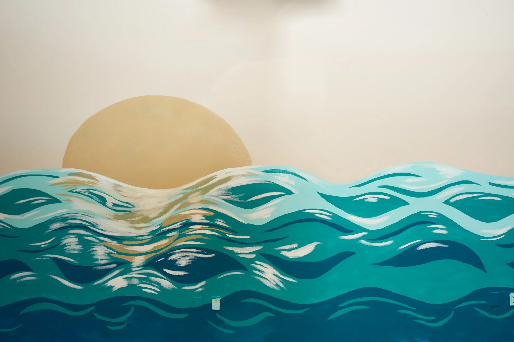 A mural of stylized ocean waves painted on a wall, with a yellow sun or moon partially visible in the background.