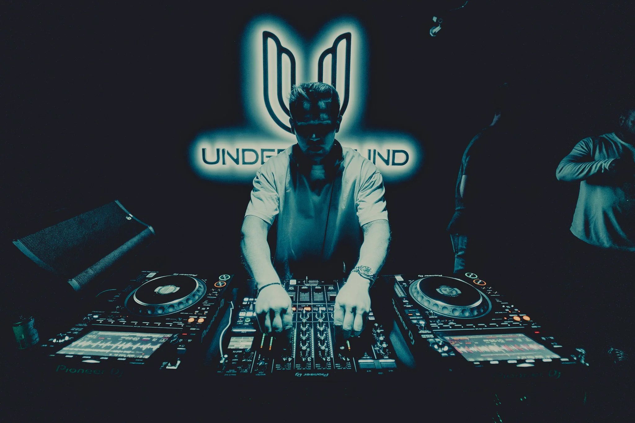 DJ performing at a club with a neon sign reading 'UNDERGROUND' behind him