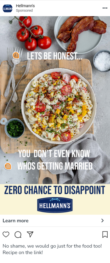 A plate of colorful pasta salad with cherry tomatoes, yellow bell peppers, and herbs, accompanied by cherry tomatoes on the vine, cooked bacon, a small bowl of chopped herbs, and salt on a gray surface, with cutlery and a napkin.